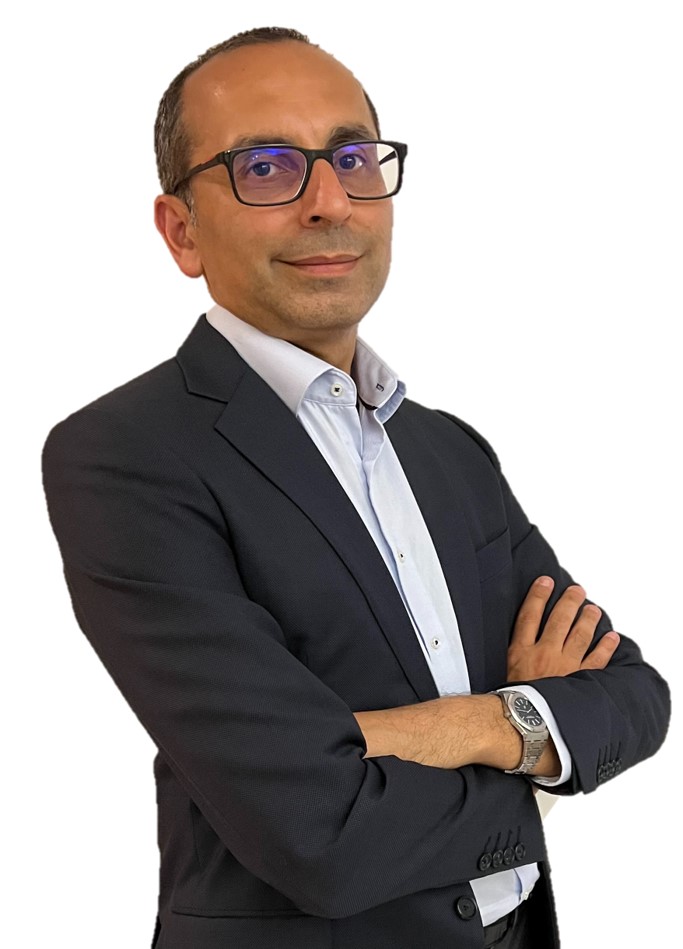 Man with glasses wearing a black suit and white shirt, arms crossed, smiling slightly, against white background.