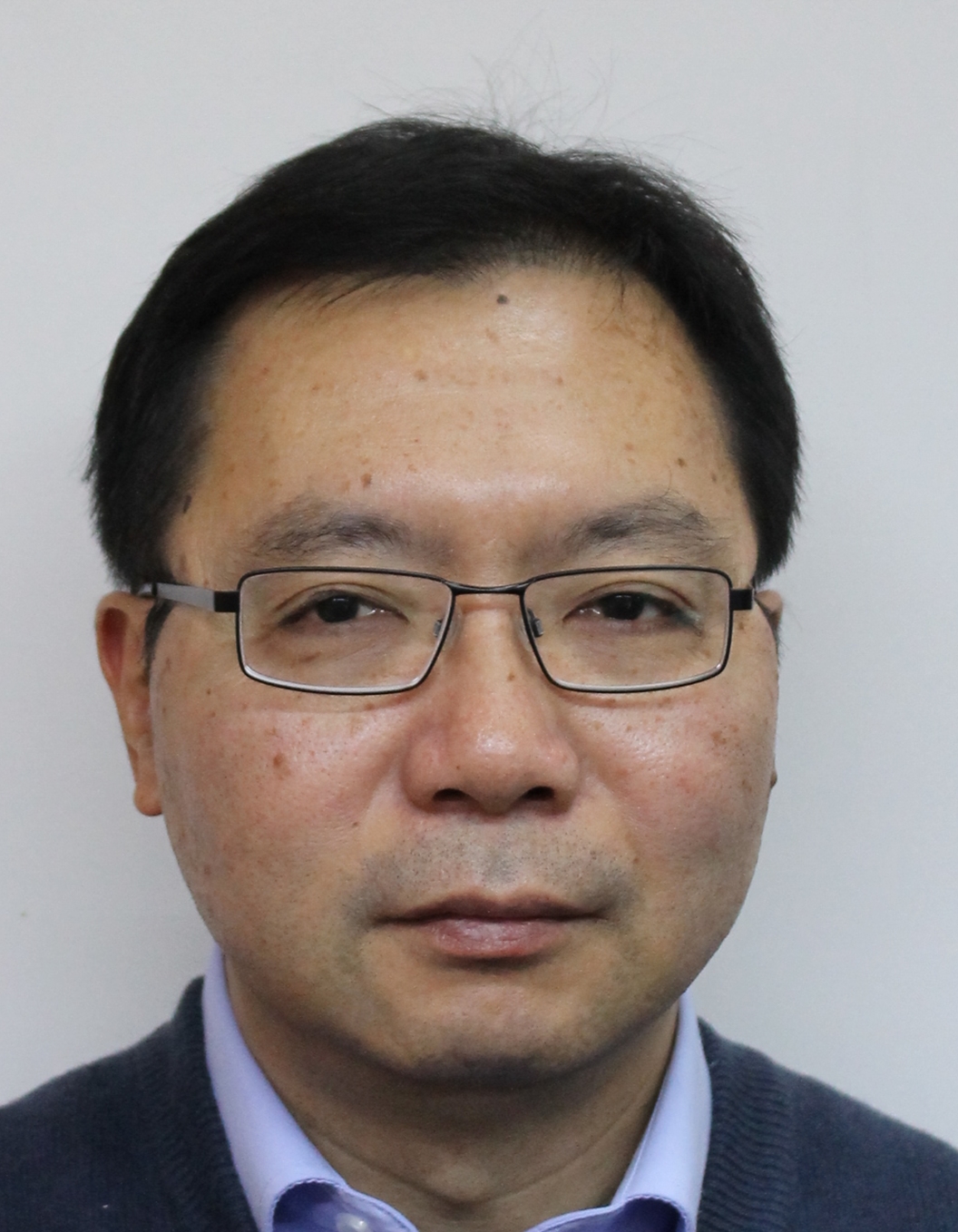 Close-up of a middle-aged man with black hair, wearing glasses, a blue shirt, and a dark sweater.