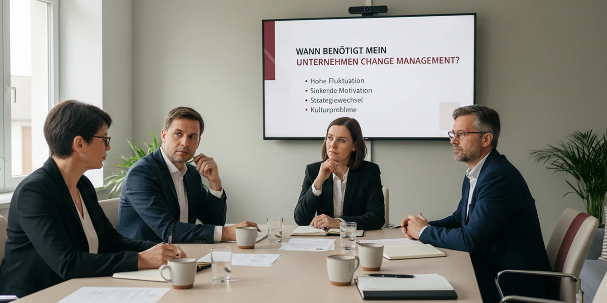 Vier Führungskräfte sitzen im Besprechungsraum vor einer Präsentation mit der Frage „Wann benötigt mein Unternehmen Change Management?“ und Stichpunkten zu hoher Fluktuation, sinkender Motivation, Strategiewechsel und Kulturproblemen.