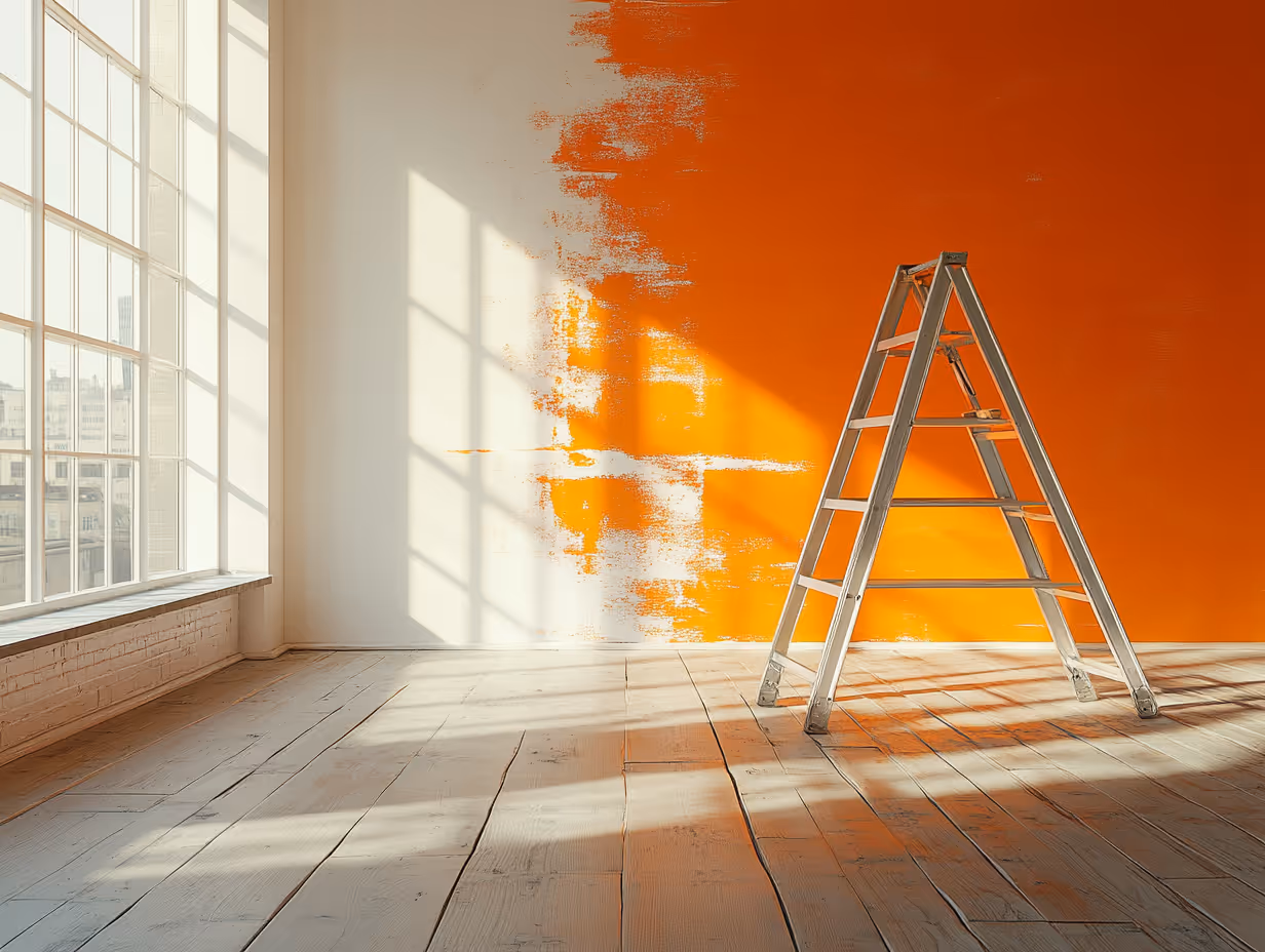 Metal ladder in a sunlit room with a wooden floor and a partially painted orange wall.