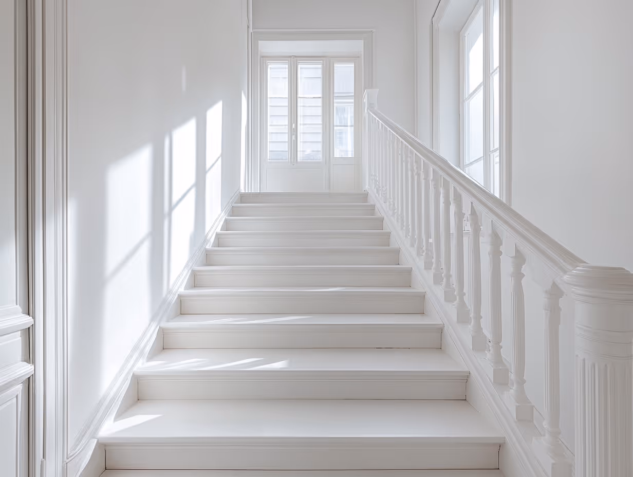 Bright white staircase with decorative railing and sunlight casting window shadows on walls.