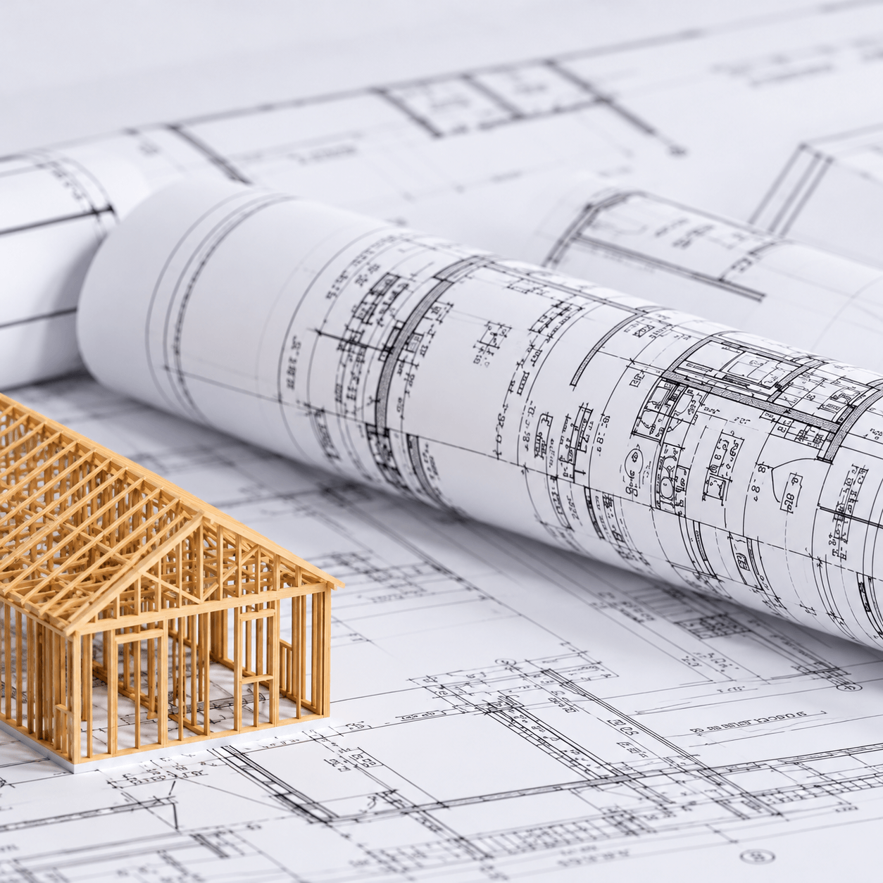 Architectural blueprints with a miniature wooden building frame, representing construction planning, engineering, and early career opportunities in the construction industry.