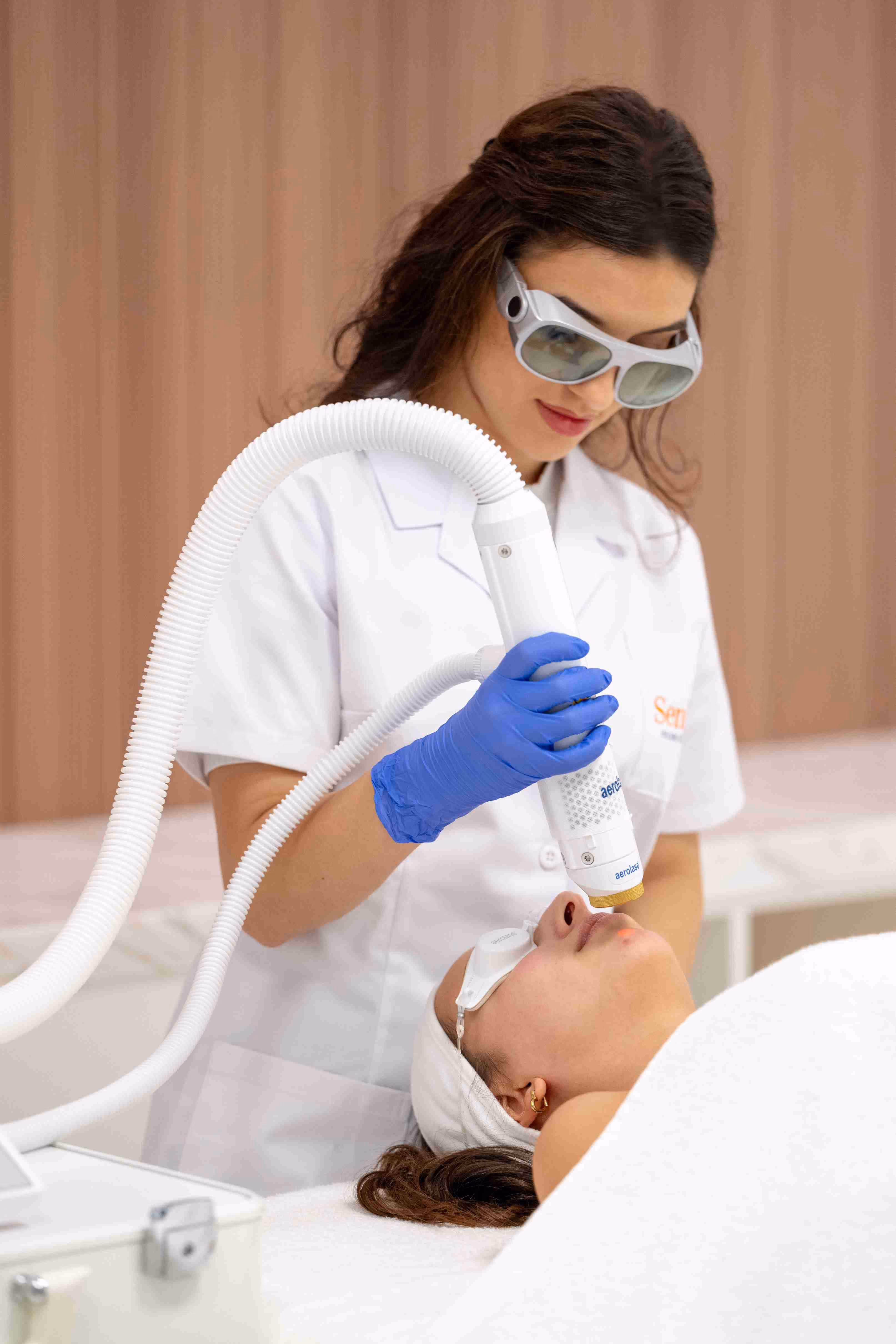 A woman in a white lab coat and goggles using a blow dryer on