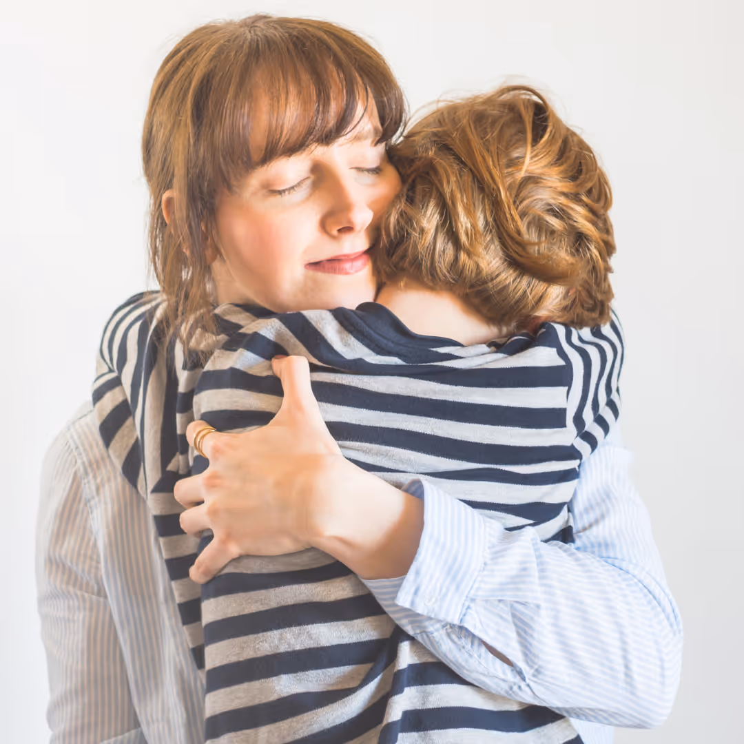 Mutter umarmt Kind in gestreiftem Shirt - warmer, inniger Moment zwischen Elternteil und Kind