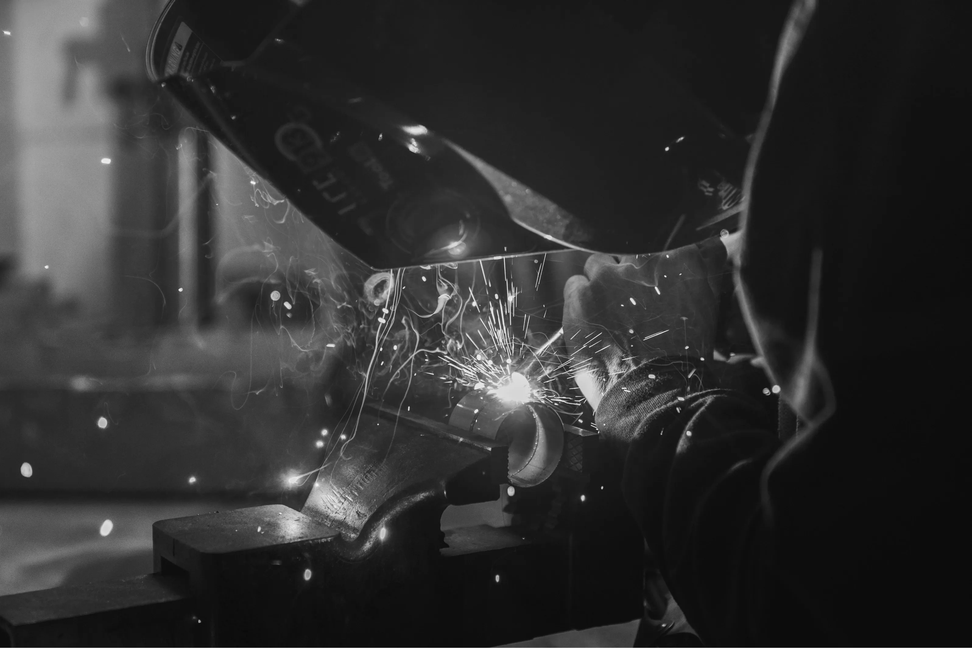 A black and white photograph showing sparks flying while a metal pipe is being welded.
