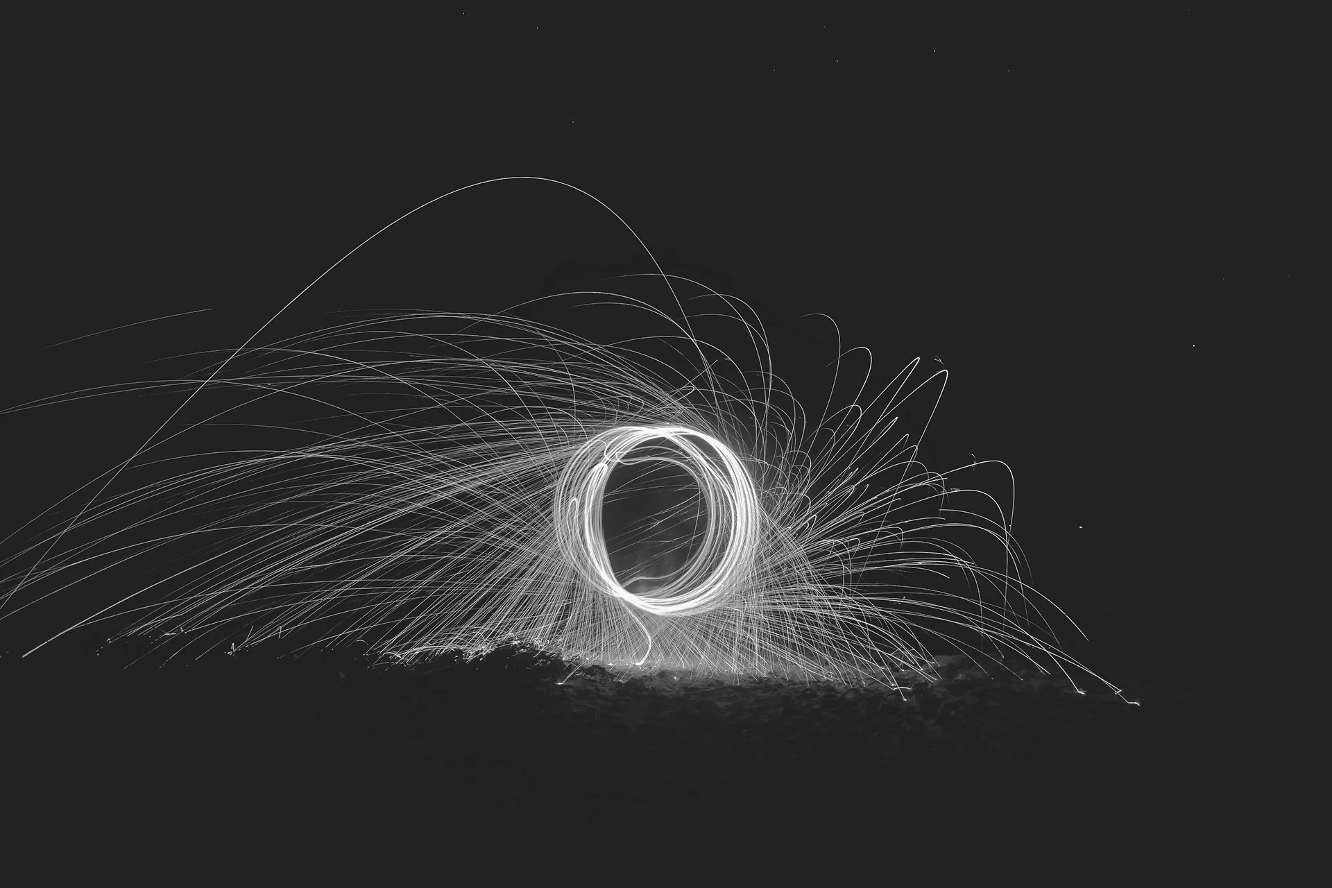 A black and white photograph showing sparks flying while a metal pipe is being welded.