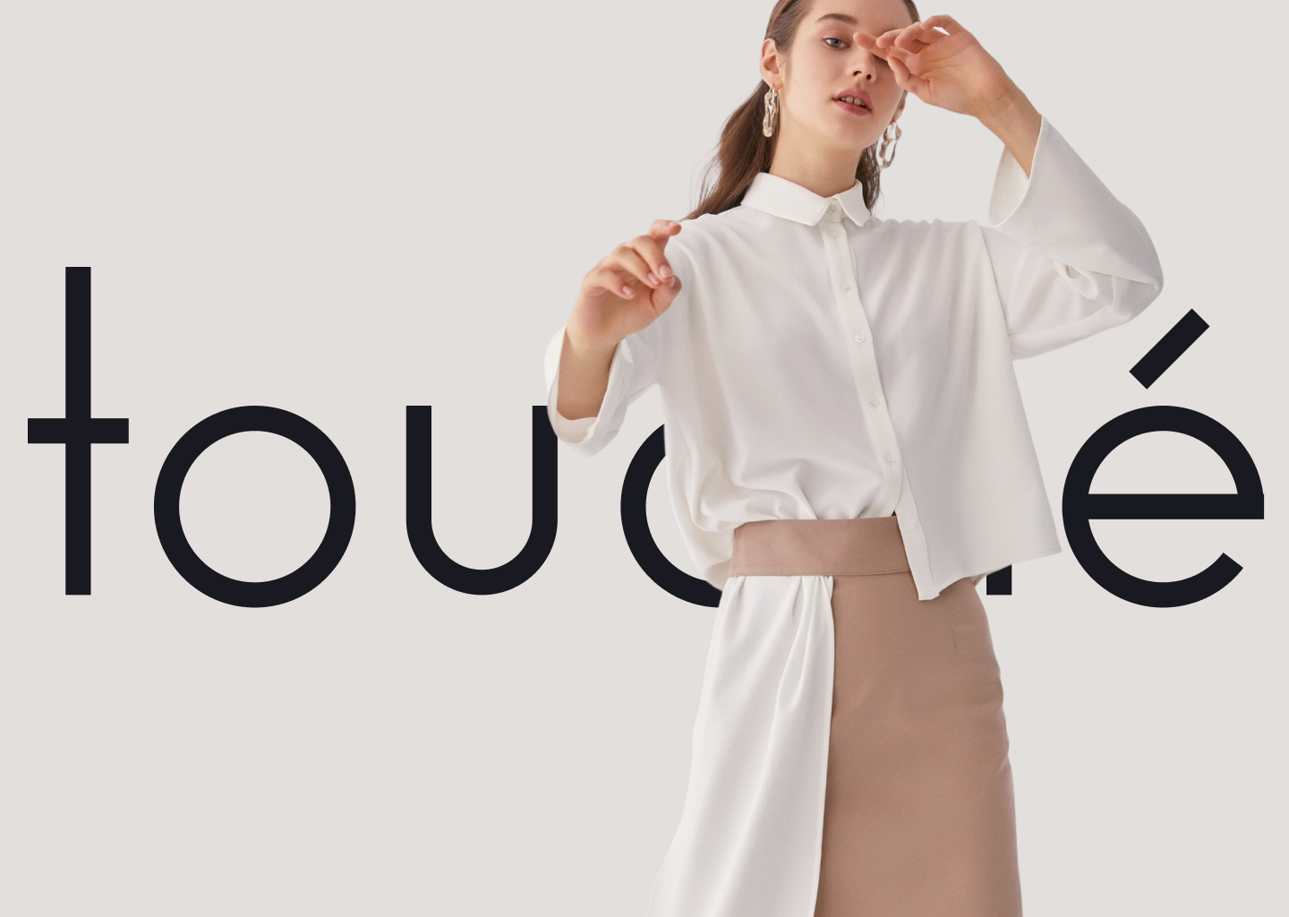 Touché wordmark with a model in a white shirt and camel skirt