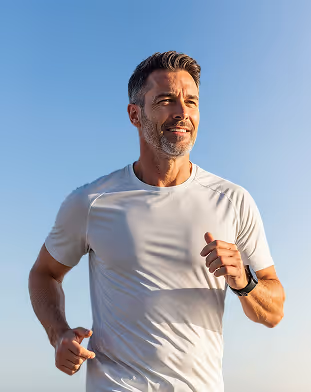 Middle-aged man jogging outdoors wearing a white t-shirt against a clear blue sky.
