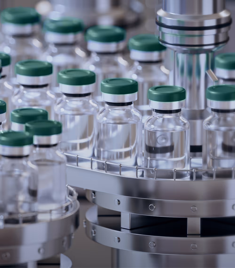 Rows of clear medication vials with green caps moving through a stainless steel automated filling machine.