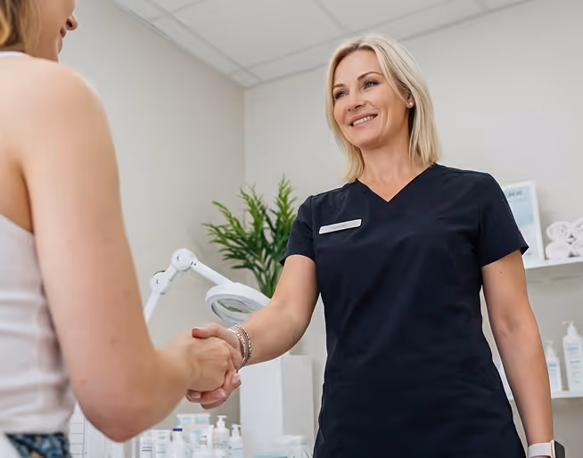 A female healthcare professional in black scrubs shaking hands with a seated patient in a clinical setting.