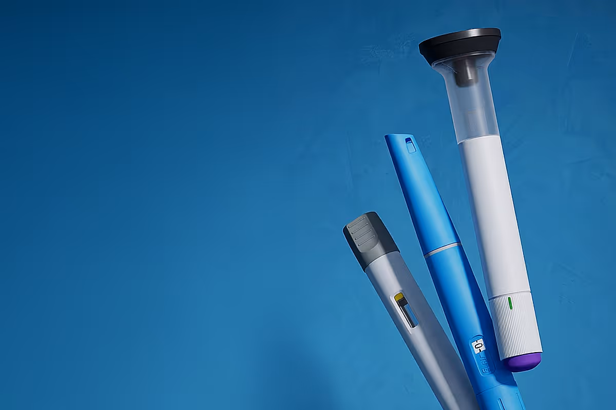 Three GLP-1 pens in different colors and designs against a blue background.