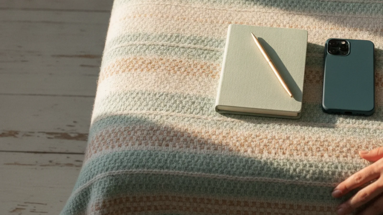 A notebook and a phone side by side on a blanket in warm afternoon light
