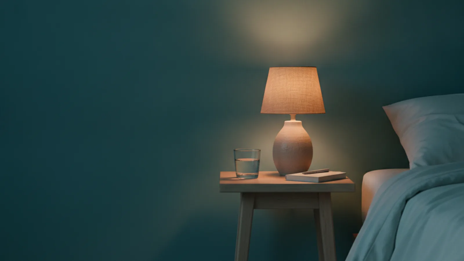 A bedside table at night with a warm lamp, a glass of water and a notebook