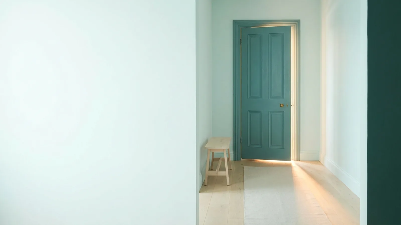 A teal door standing slightly ajar with warm morning light spilling across a pale wooden floor