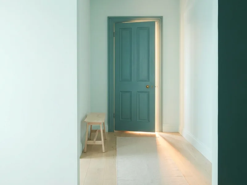 A teal door standing slightly ajar with warm morning light spilling across a pale wooden floor