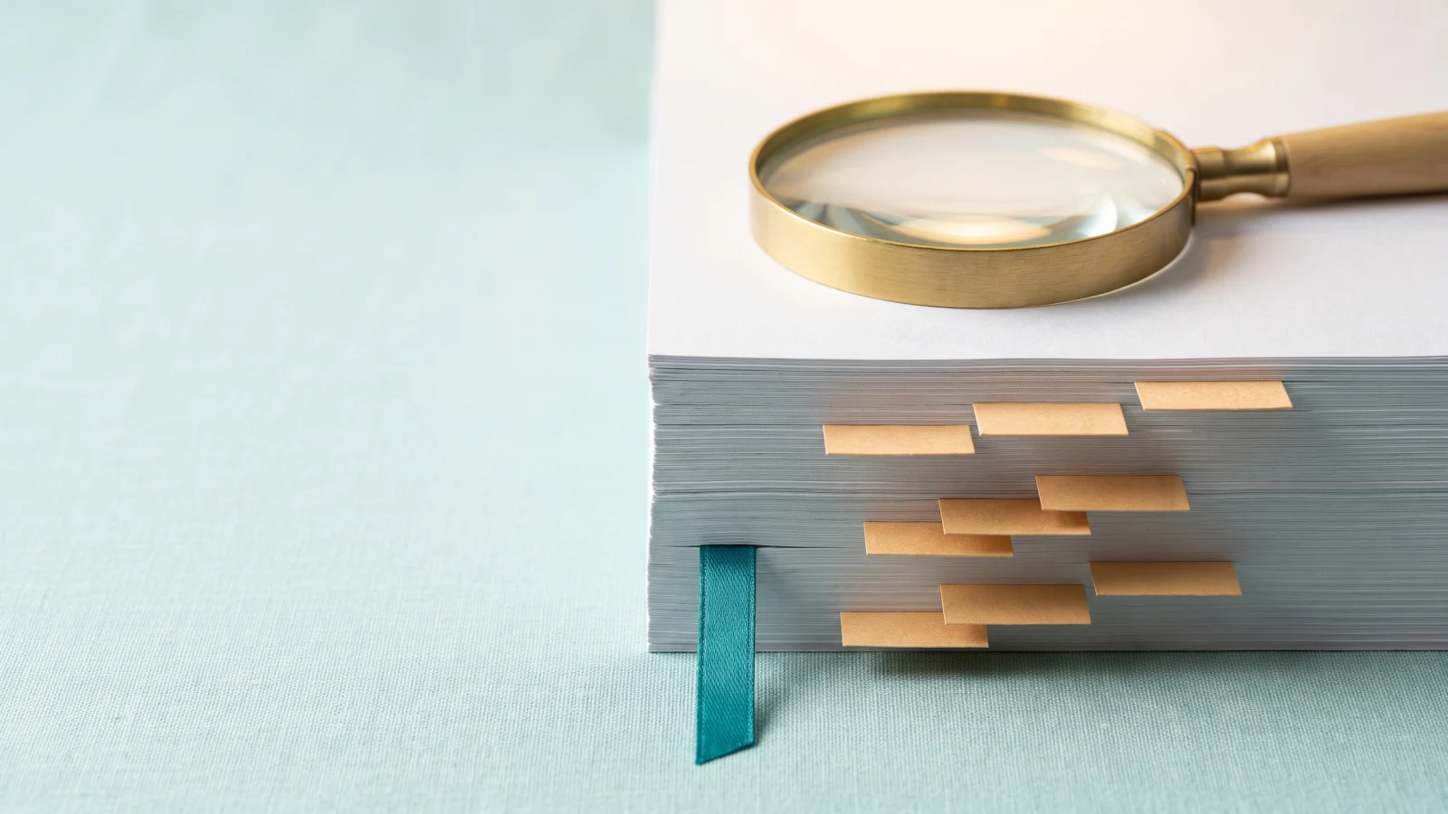 Brass magnifying glass on a thick stack of blank pages with small sand-coloured tabs marking different depths