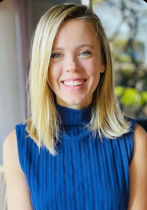 Smiling woman with straight blonde hair wearing a sleeveless blue ribbed top.