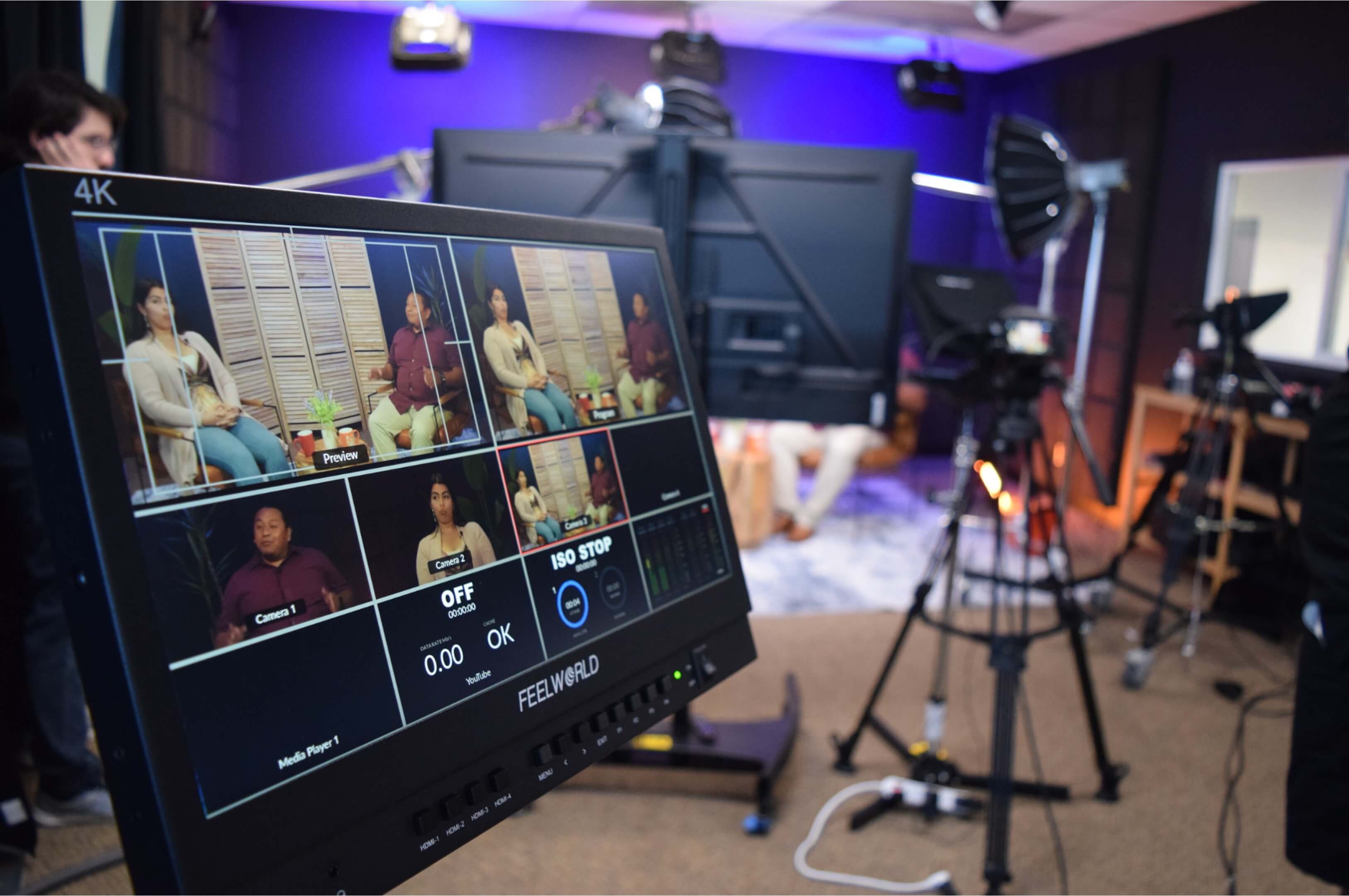Photo shows camera equipment set up in the studio with a TV close-up showing the video feed.
