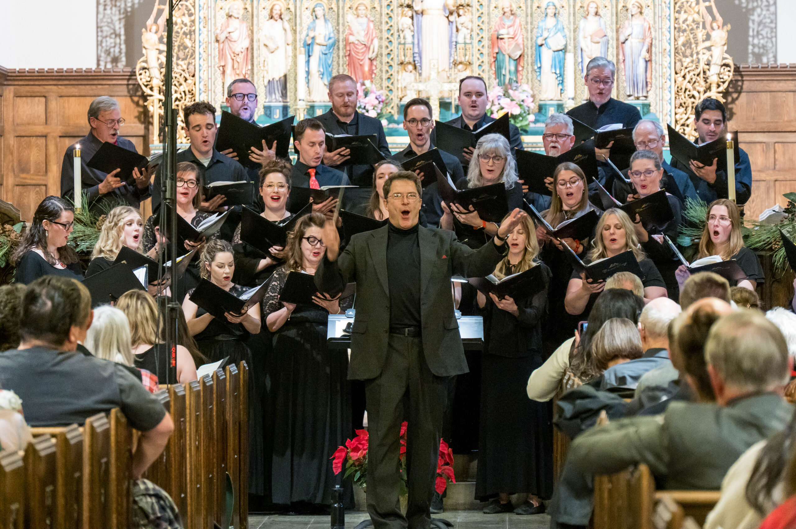 Choir performing under conductor's direction in a church with religious statues in the background.