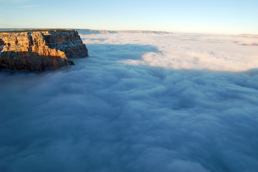 Acantilados del Gran Cañón iluminados por el sol sobre un extenso mar de nubes.