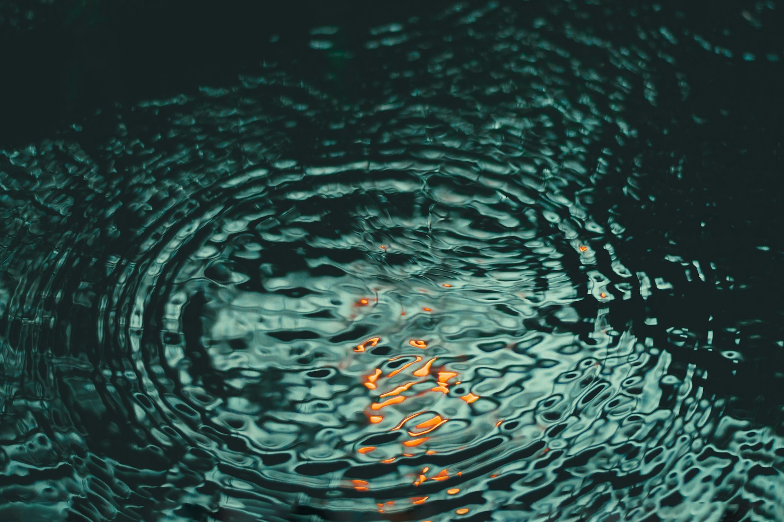 Ondas concéntricas sobre agua verde profunda, con pequeños reflejos dorados.