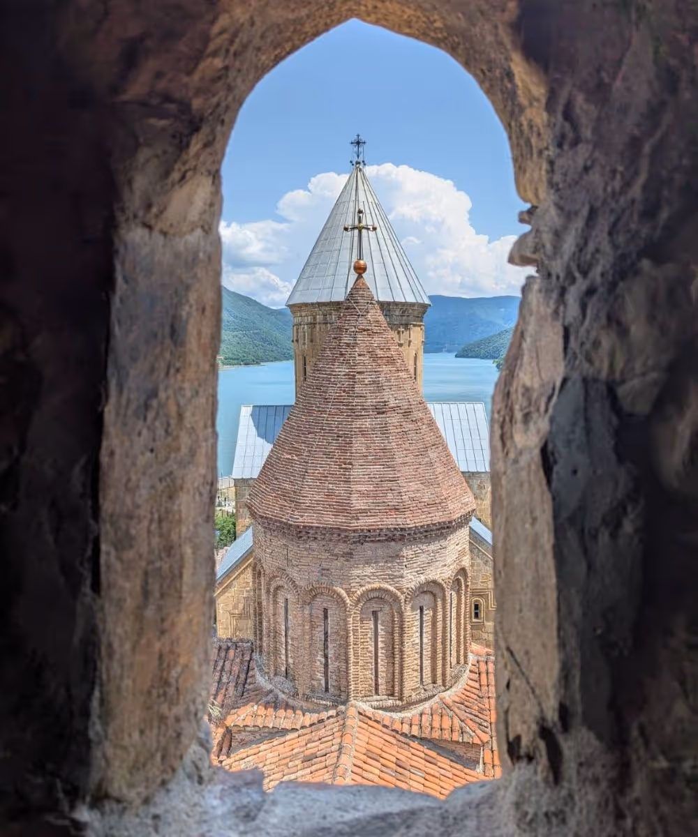 The towers of Ananuri Fortress seen through a stone window arch overlooking the Zhinvali Reservoir in Georgia.