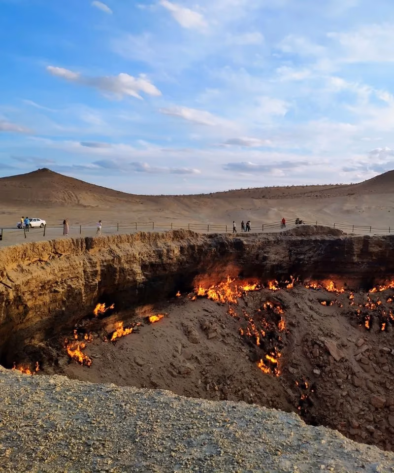 The burning Darvaza Gas Crater (Gates of Hell) in the Karakum Desert of Turkmenistan with visitors standing along the rim.