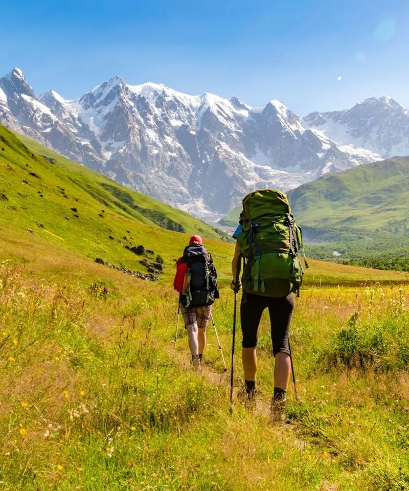 Two hikers backpacking through the lush green valleys of Svaneti in the Caucasus mountains of Georgia.
