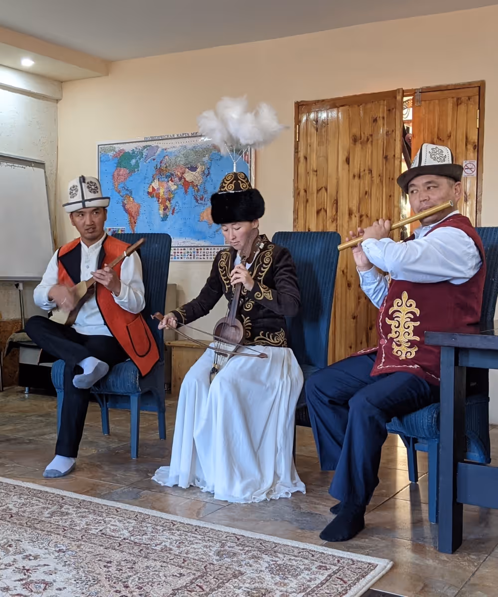 Three musicians dressed in traditional Kyrgyz national costumes performing folk music using traditional instruments.