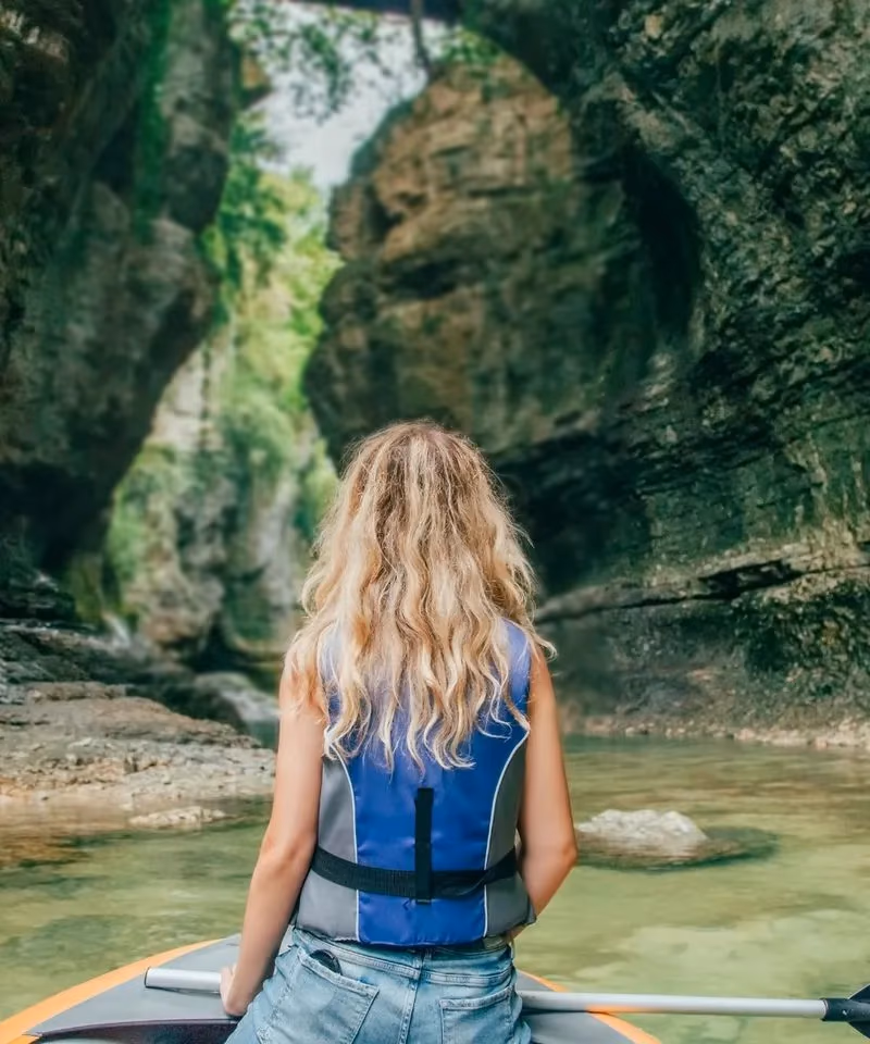 A woman wearing a life jacket paddling a kayak through the towering rocky cliffs of a beautiful canyon in Georgia.