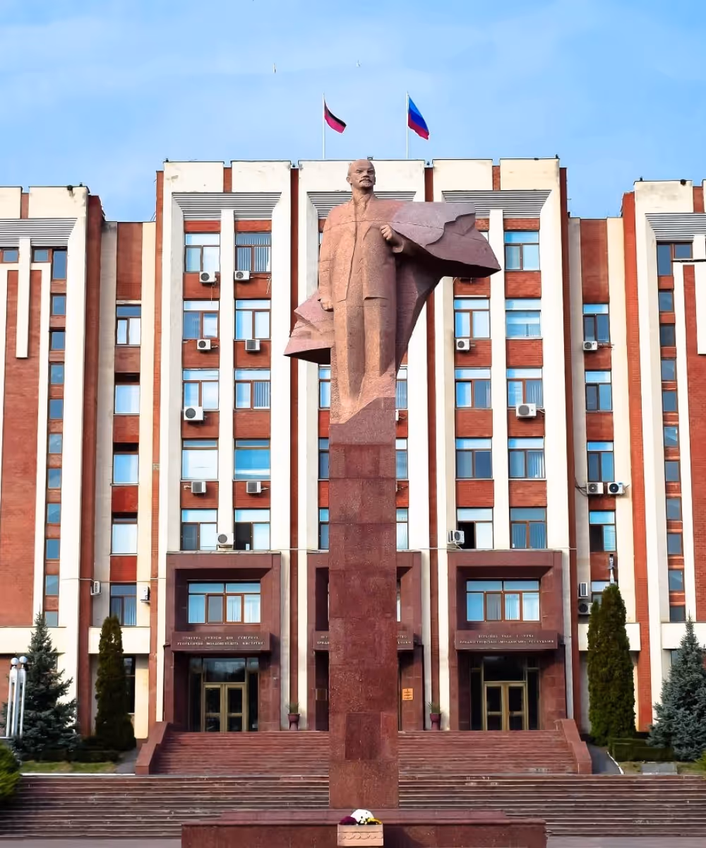 The red granite statue of Vladimir Lenin standing on a tall column in front of the Transnistrian Parliament building in Tiraspol.