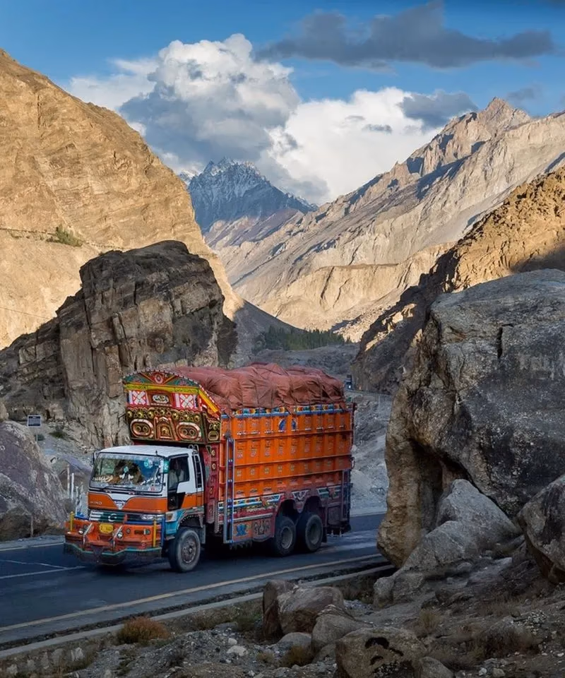A brightly decorated Pakistani truck with traditional truck art driving along a paved mountain road in Northern Pakistan.