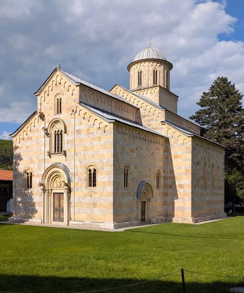 The medieval Serbian Orthodox Visoki Decani Monastery standing on a green lawn under a blue sky in Kosovo.