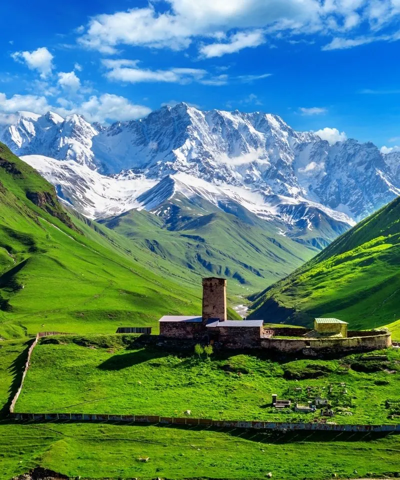 Lamaria Church and Svan tower in Ushguli, Georgia, beneath the snowy peaks of Mount Shkhara.