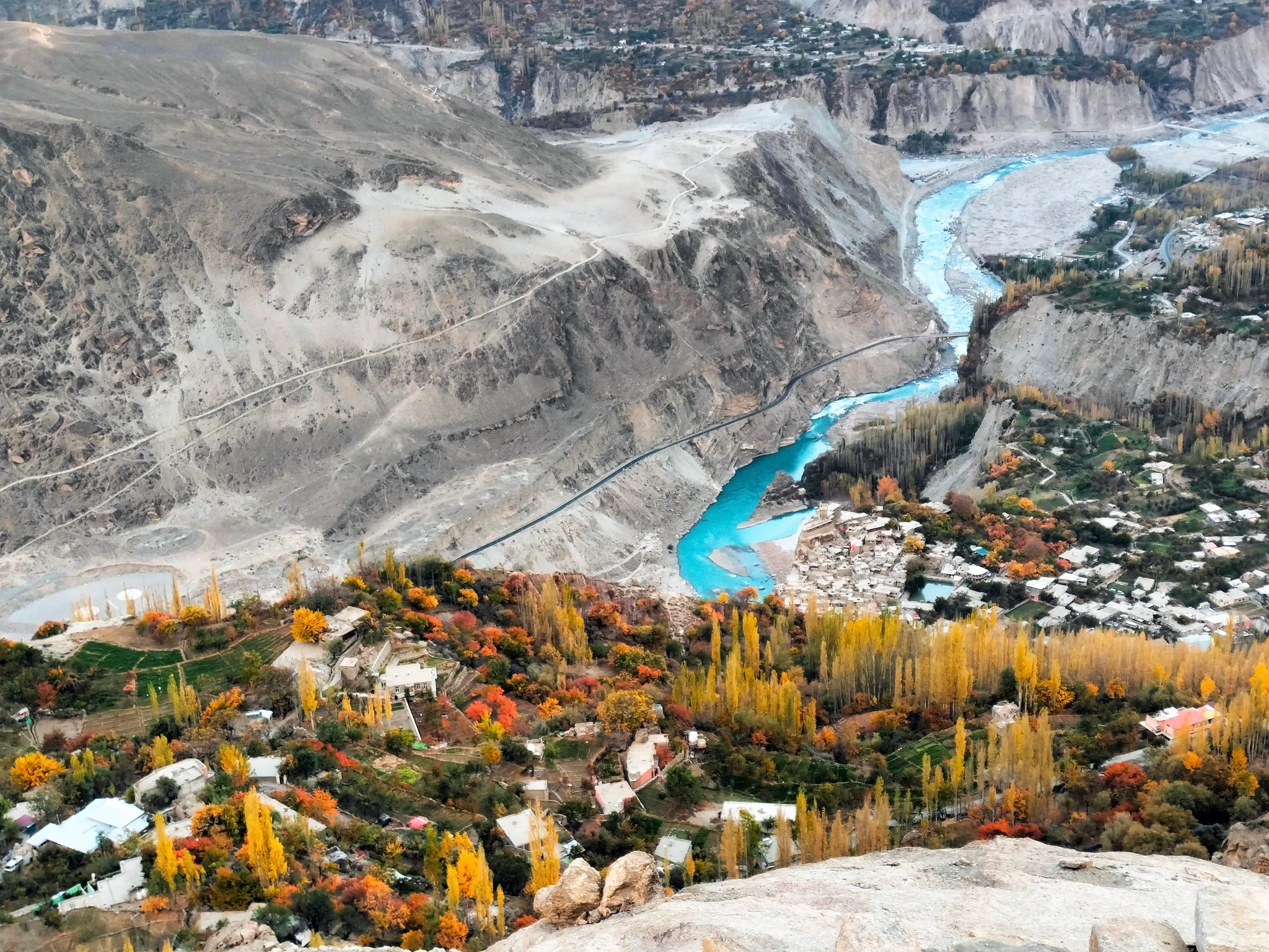 Aerial view of turquoise Hunza River winding through fall-toned valleys near Altit Fort.
