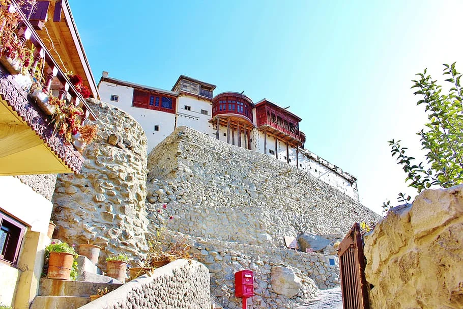 Ancient stone-walled Balti Fort rises over Skardu with vibrant flowerpots and clear blue skies.