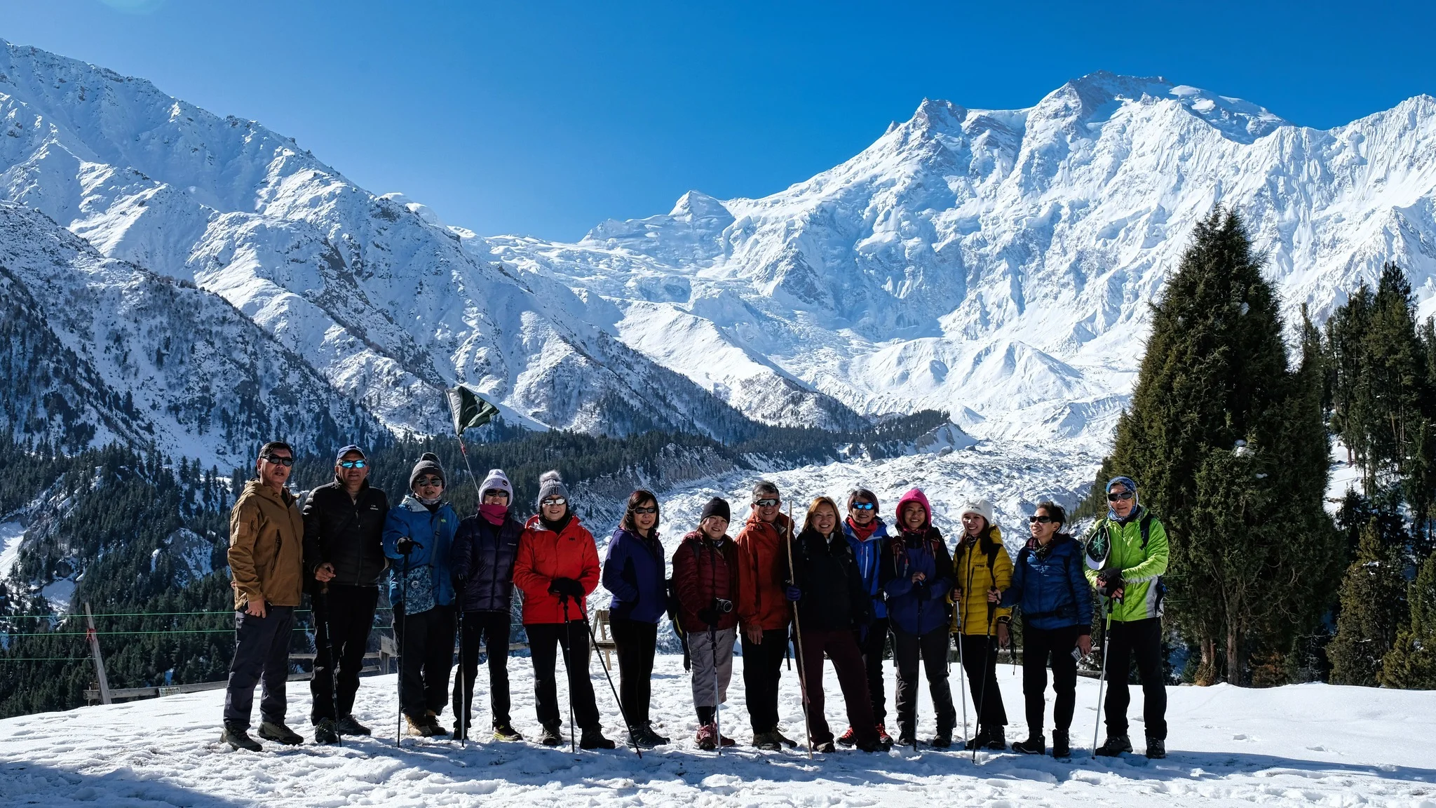 Group of hikers pose at snow-covered Fairy Meadows with Nanga Parbat towering behind.