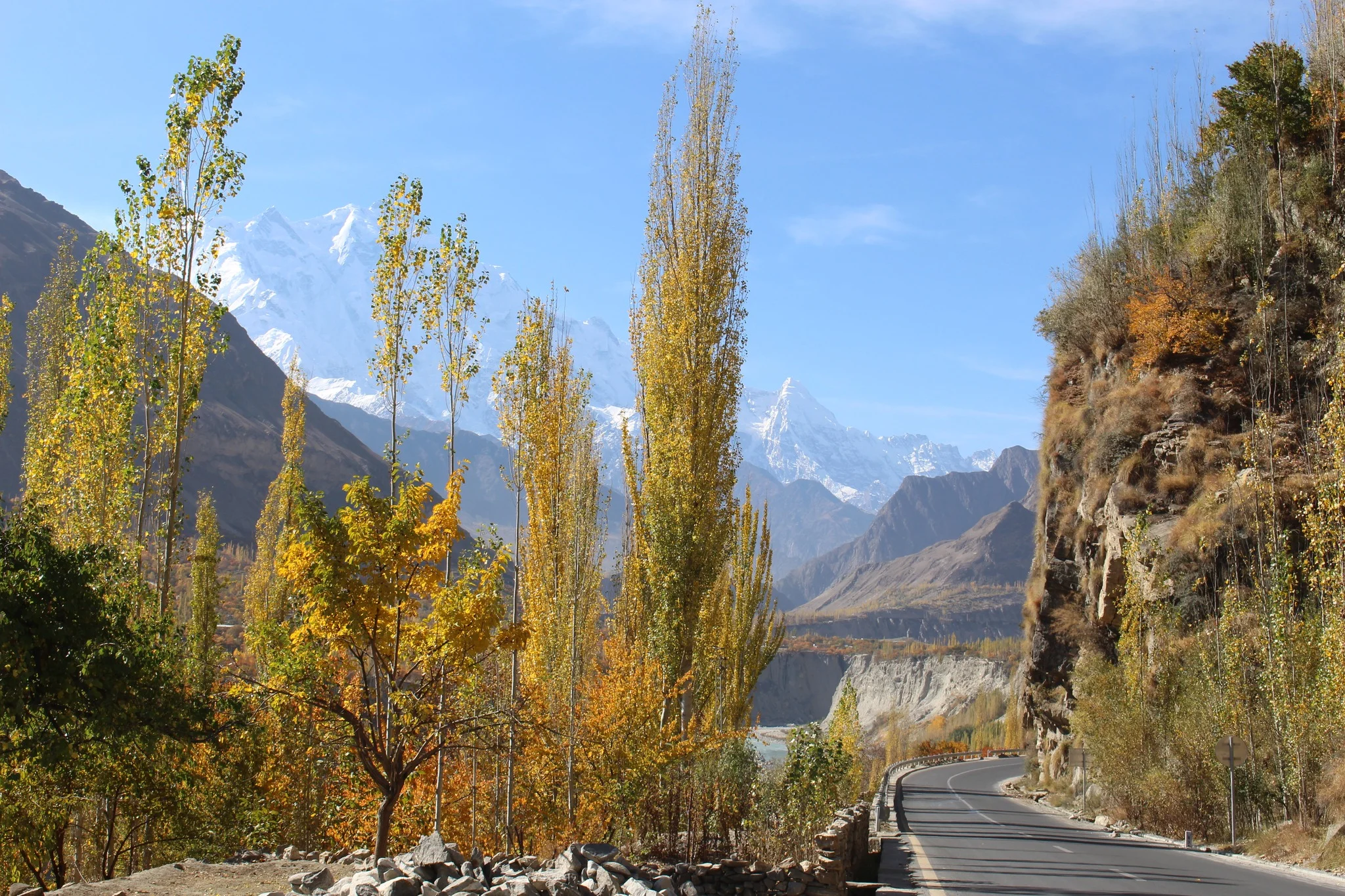 The Karakoram Highway winds between golden trees and peaks, with Rakaposhi glowing in the distance.