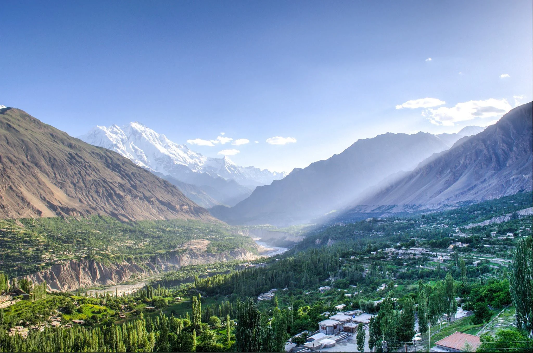 Panoramic view of Hunza Valley with lush greenery and distant Rakaposhi peak under clear skies