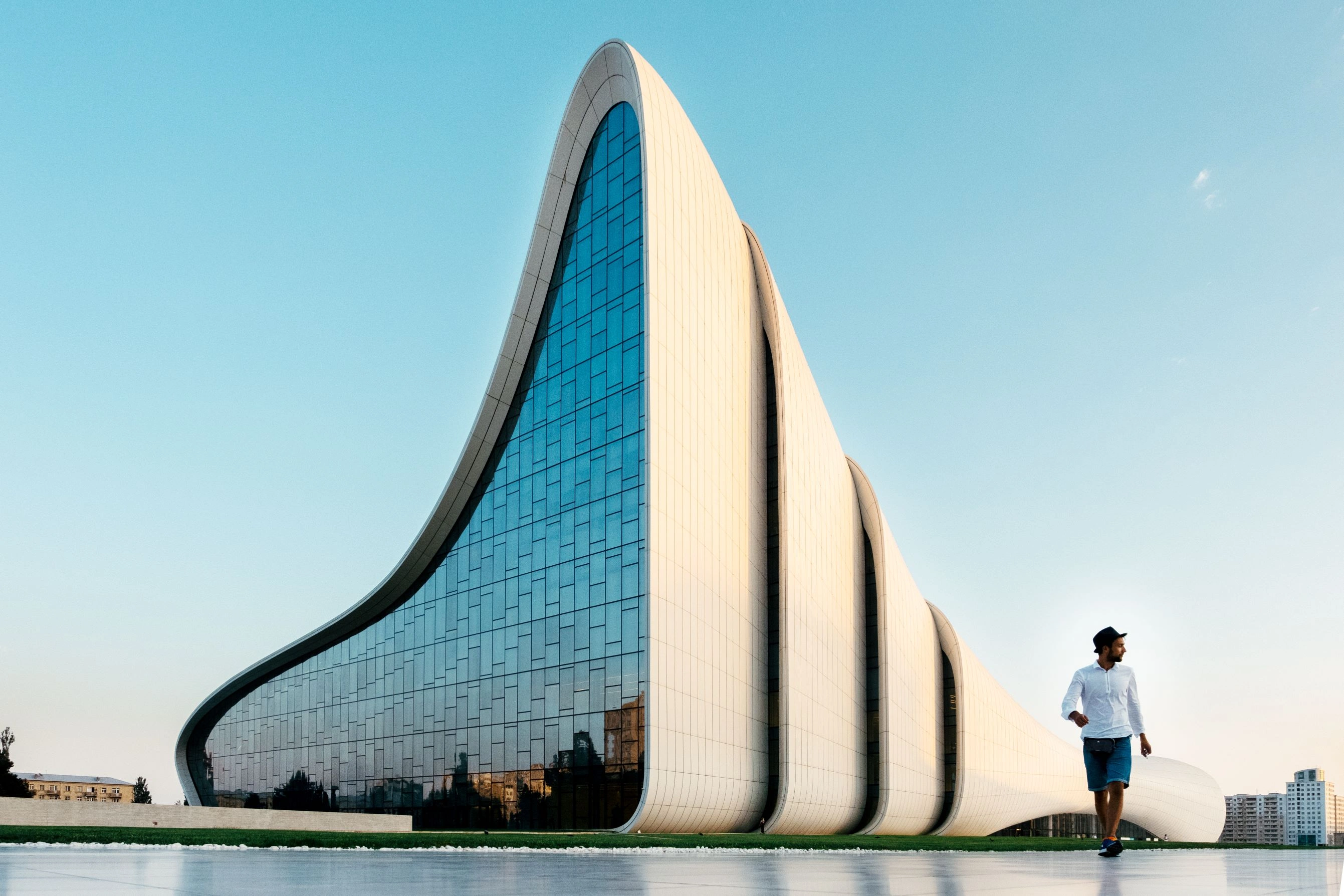 Curved, futuristic glass facade of the Heydar Aliyev Center in Baku with a man walking nearby.