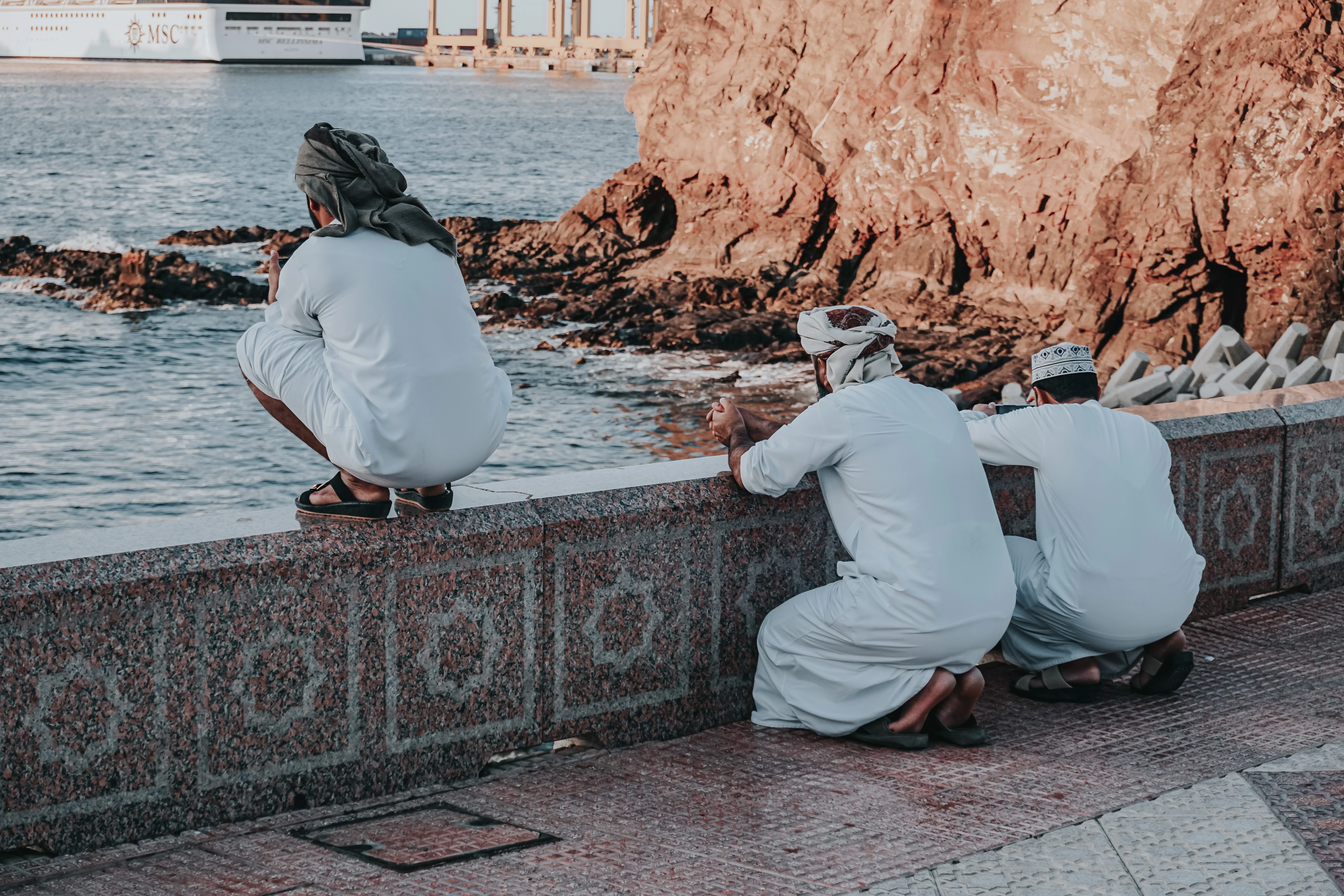 Three men in traditional Omani attire enjoying the coast on an Oman tour.