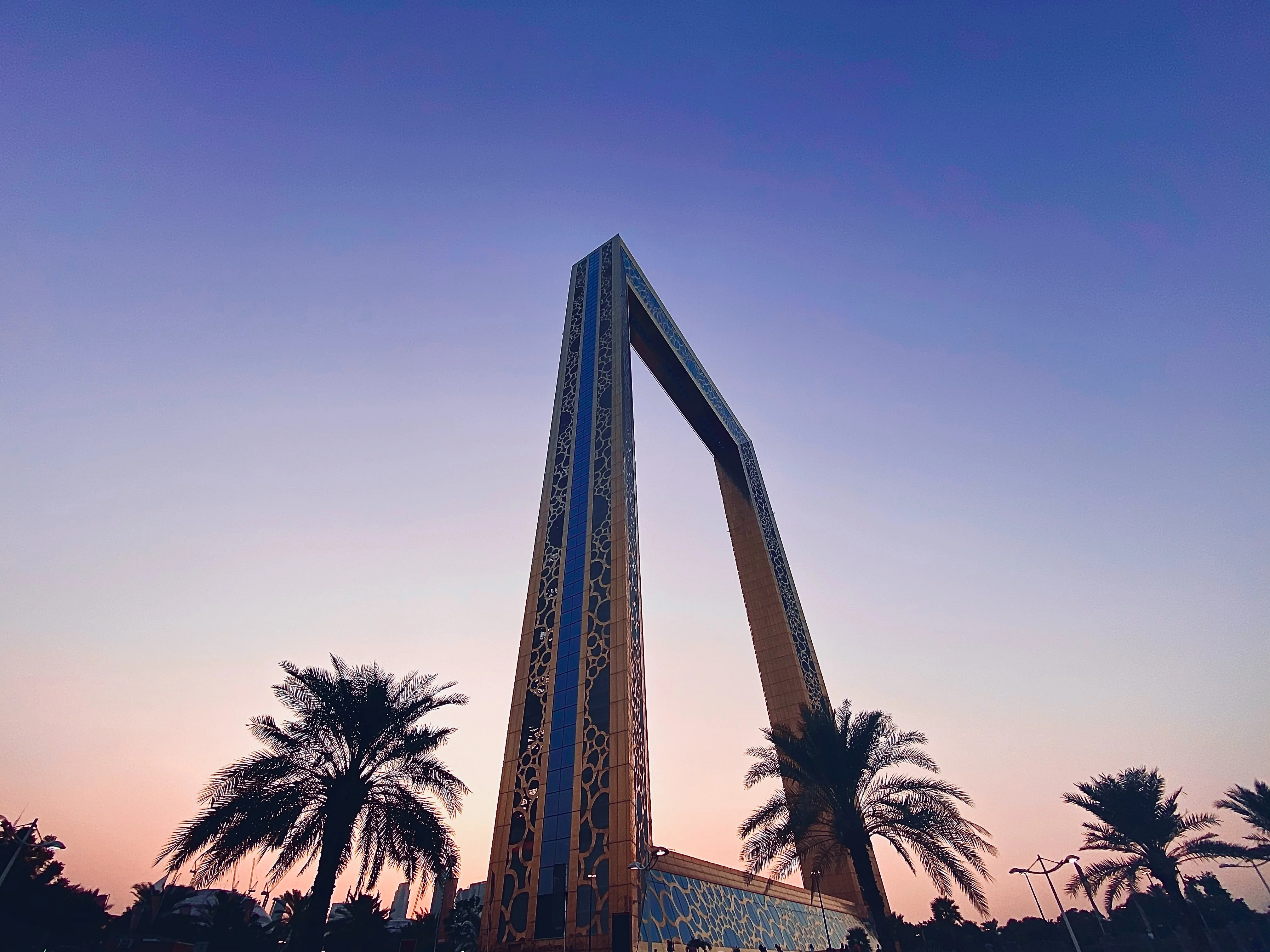 The Dubai Frame landmark at dusk with palm trees in foreground