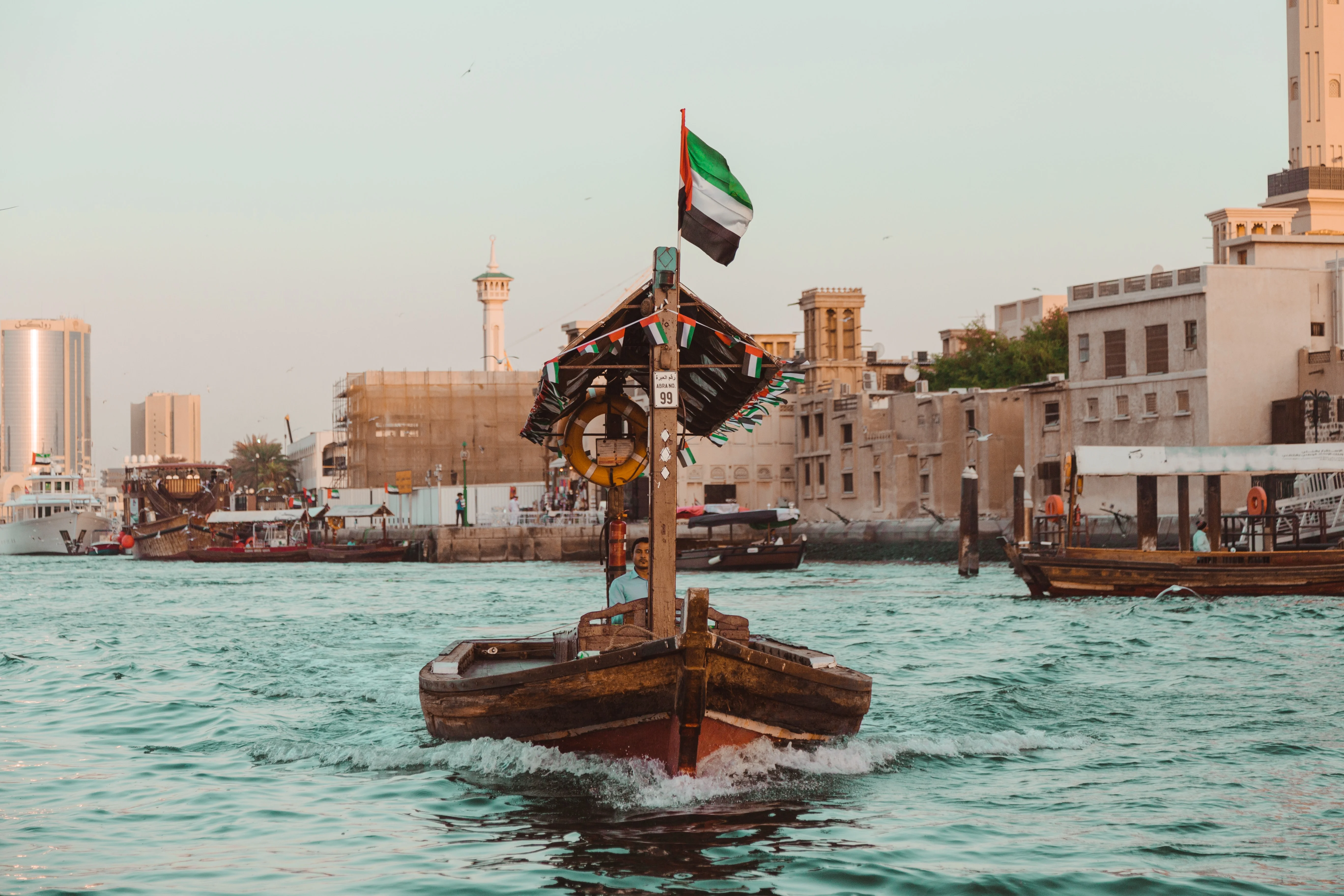 Traditional wooden abra boat sails Dubai Creek at dusk