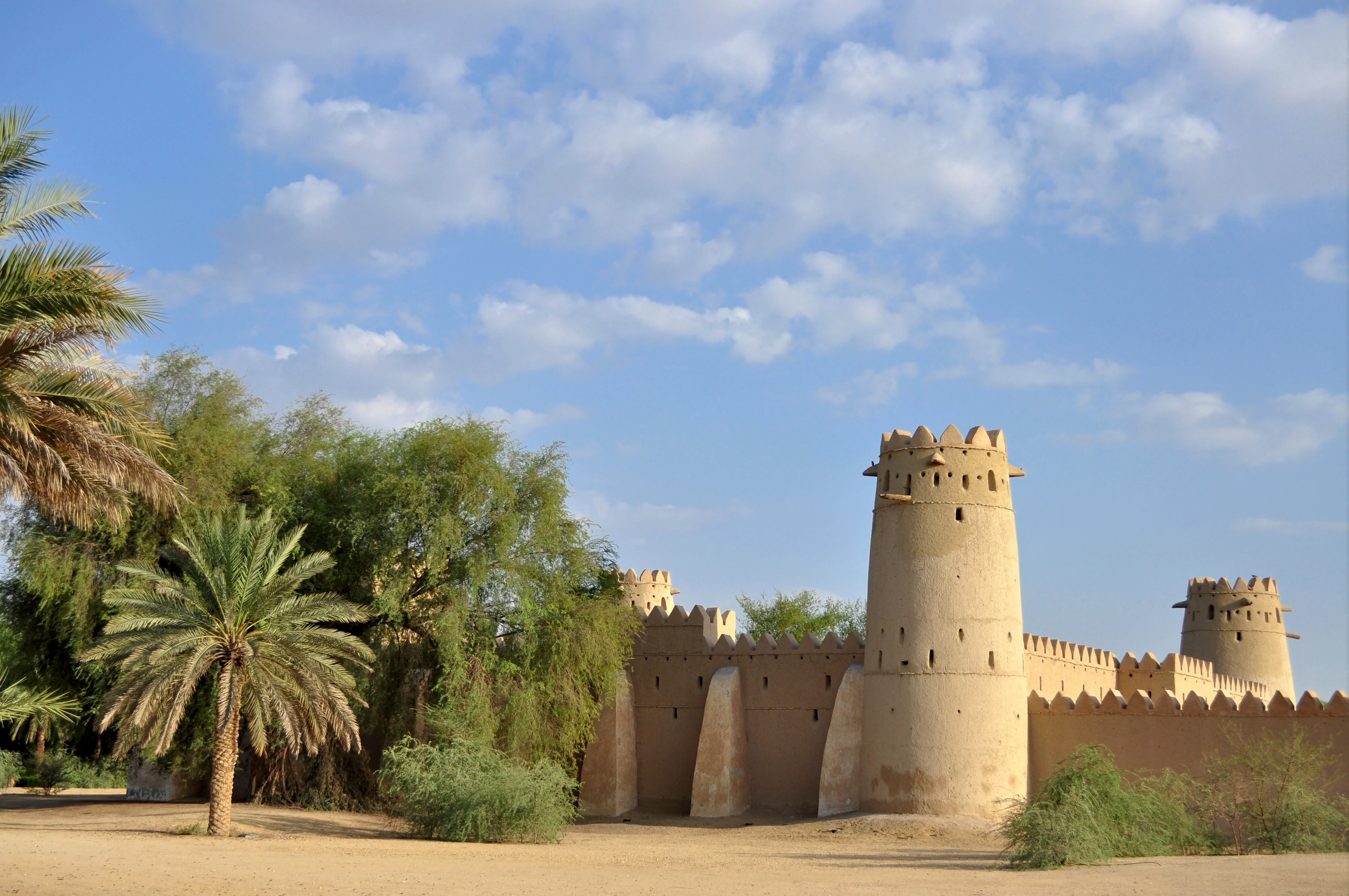 Historic Al Jahili Fort in Al Ain with palm trees under a bright sky