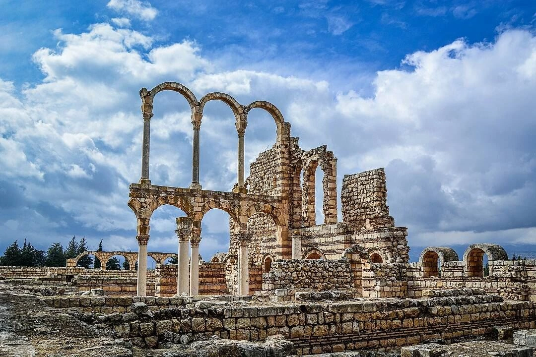Stone arches and columns of the ancient ruins in Anjar under a dramatic cloudy sky.