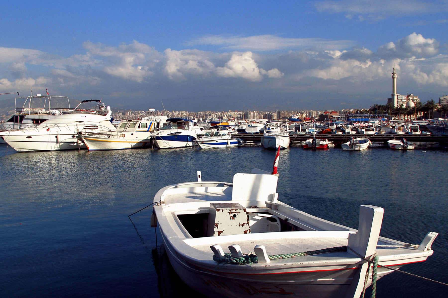 White fishing boats and yachts docked in the harbor of Tyre with the city skyline in the back.