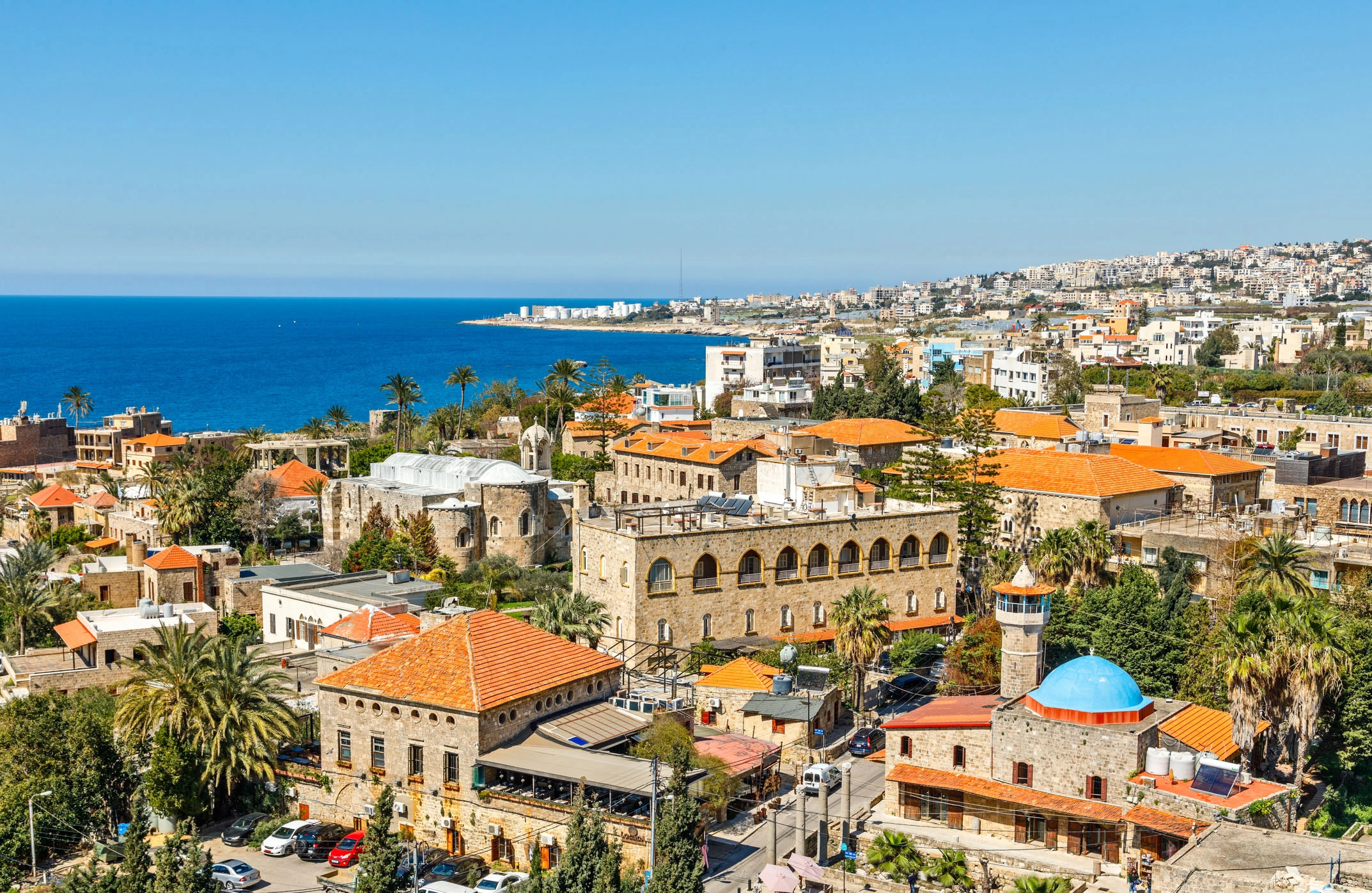 Aerial view of historic Byblos with orange rooftops and the sea stretching into the horizon.