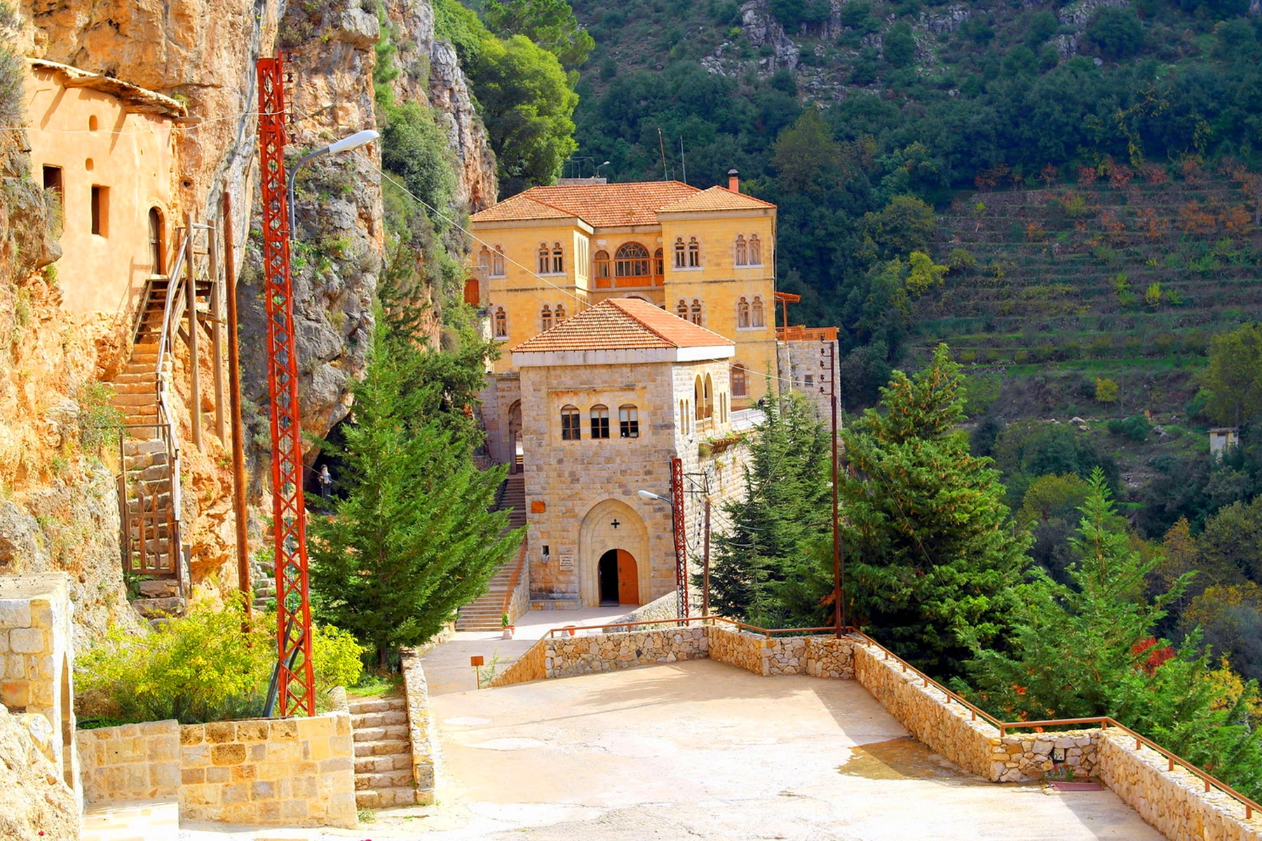 Monastery of Qannoubine nestled into rocky cliffs with stairways and pine trees.