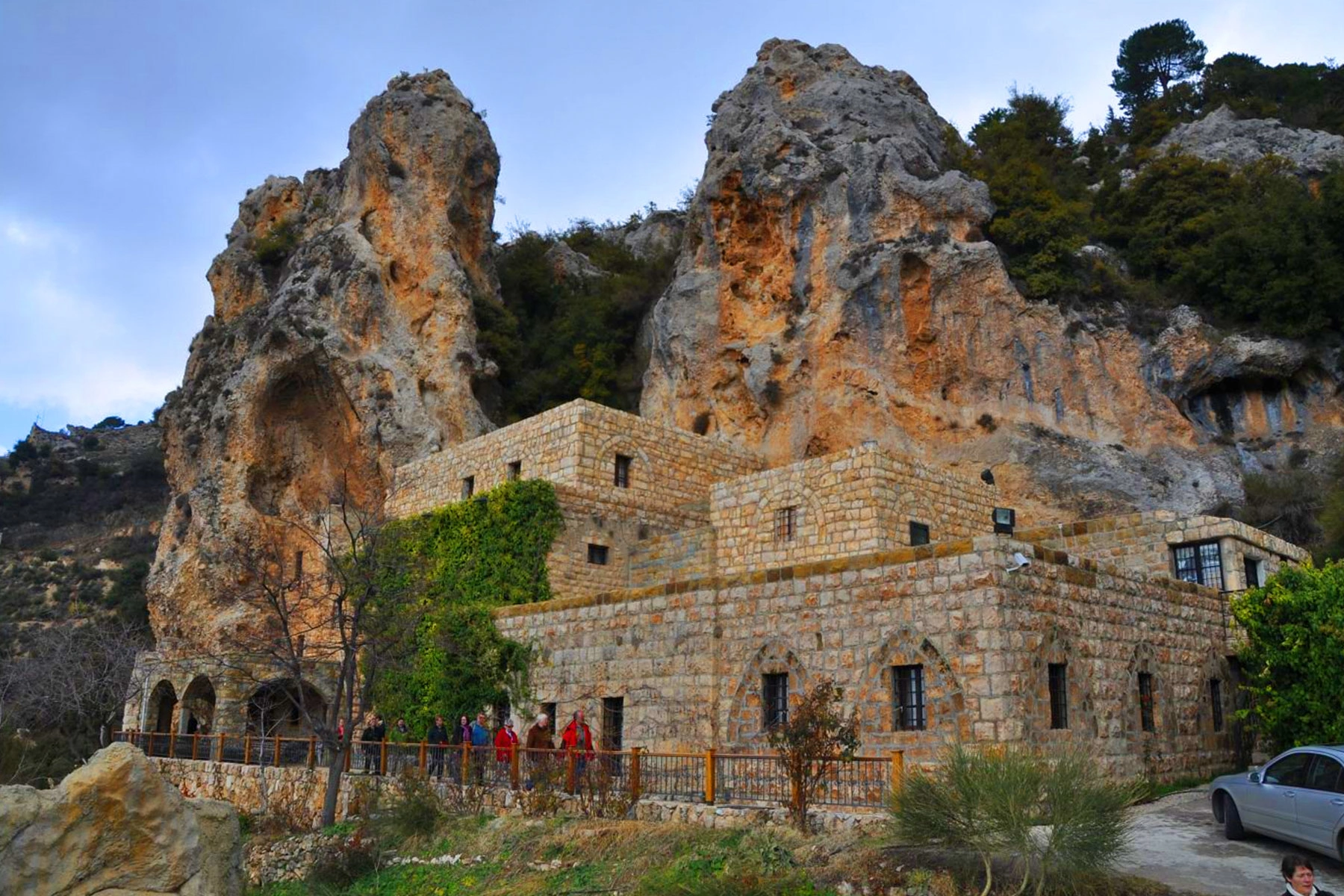 Rocky cliffside above a stone monastery building in Qozhaya Valley under a cloudy sky.