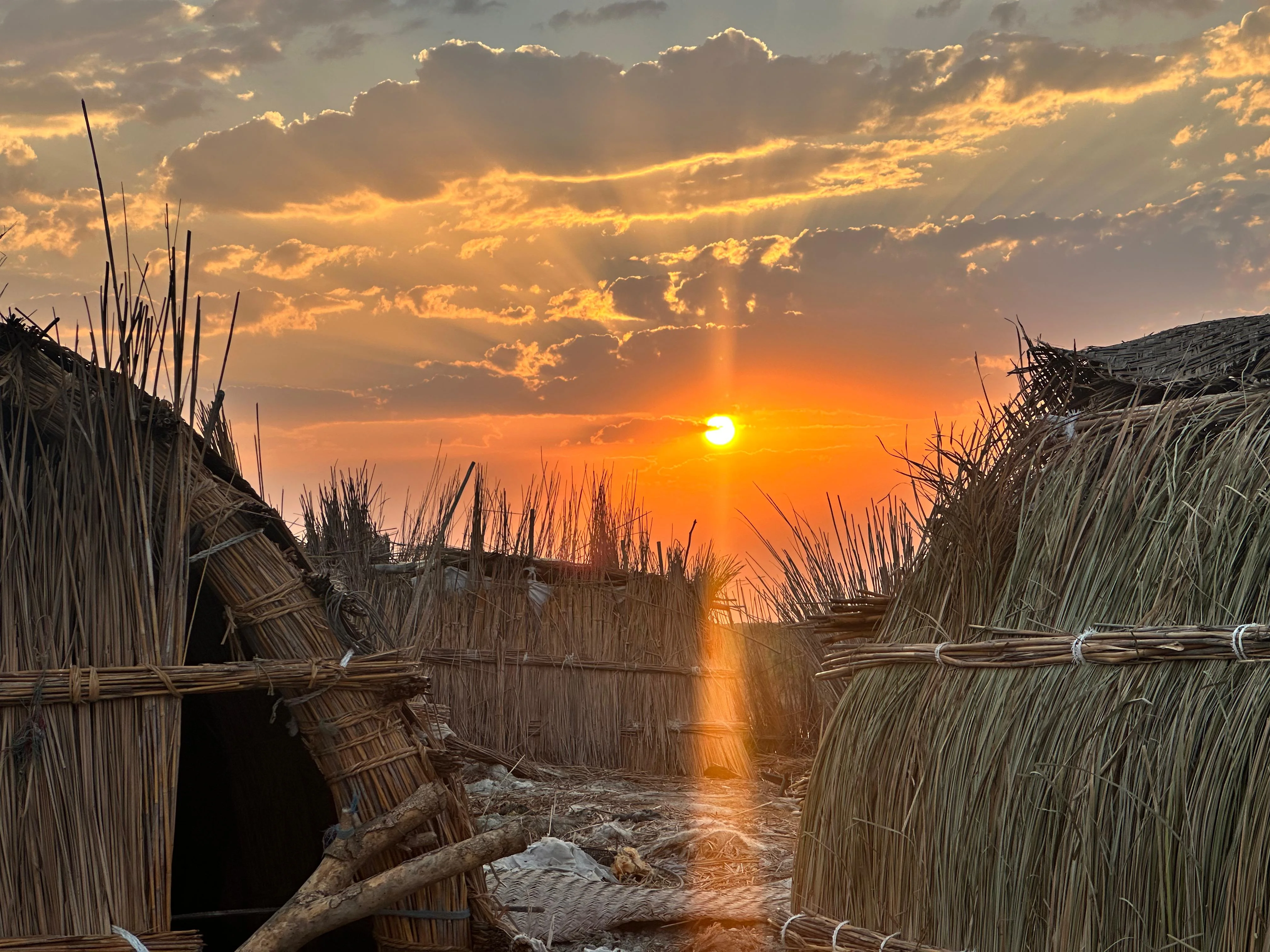 Sunset over traditional reed houses in Iraq’s Mesopotamian Marshes with golden light and clouds